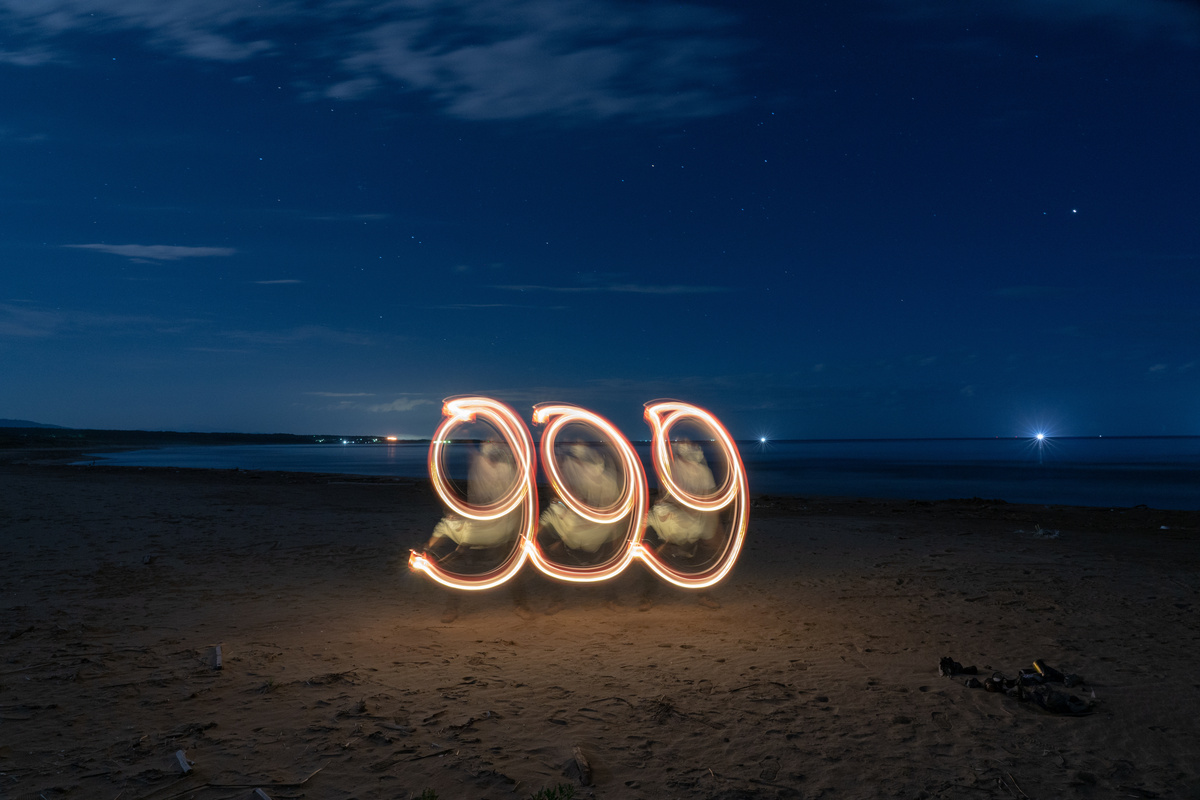 Número 999 feito por meio de luzes em uma praia.