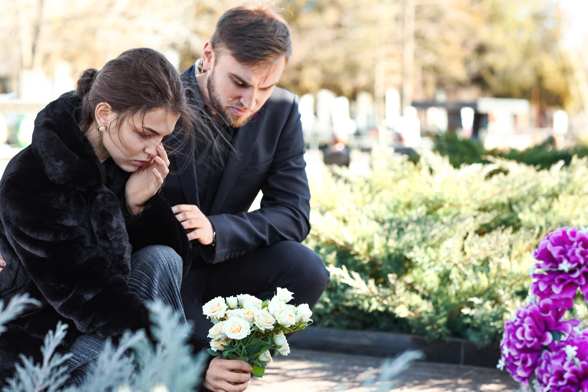 Casal de homem e mulher depositando flores em túmulo de pessoa que já morreu.