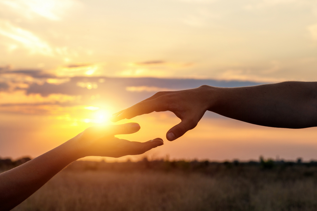 Duas mãos se encontrando em frente ao pôr do sol, simbolizando o contato com uma pessoa que já morreu.