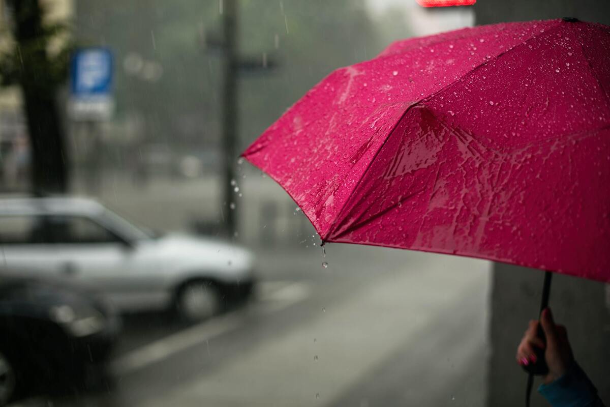 Mulher com guarda-chuva rosa, se protegendo da chuva.