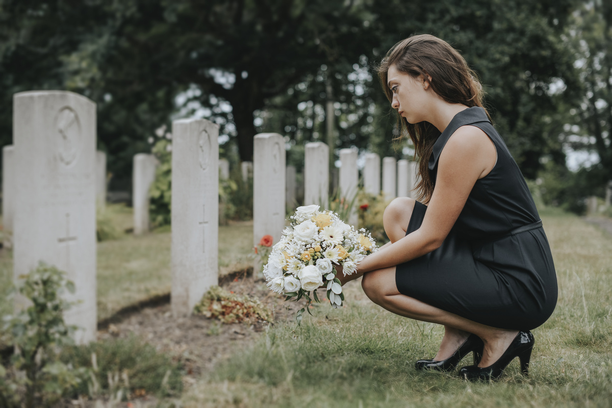 Mulher depositando flores em túmulo do marido.