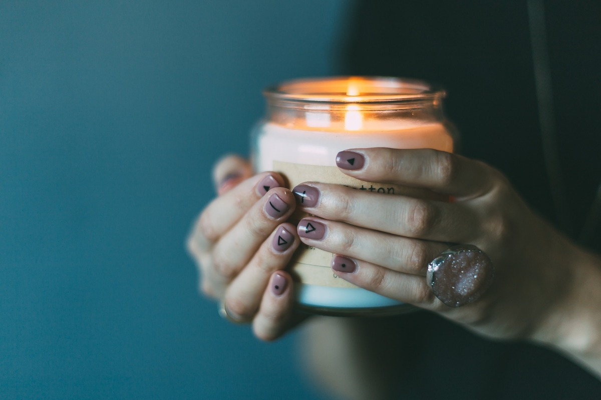 Mãos femininas segurando jarra com vela acesa dentro.