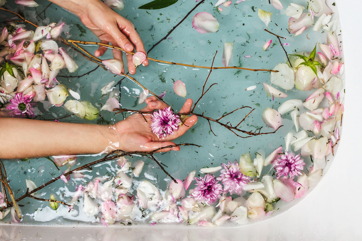Mãos femininas pegando galhos e flores em banheira