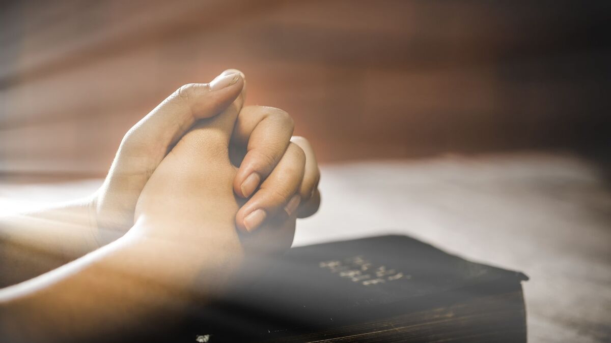 Mãos cruzadas em cima de uma bíblia.