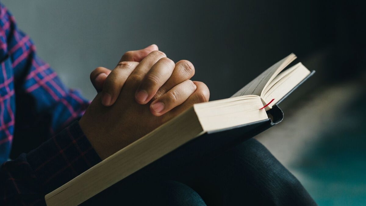 Pessoa lendo a bíblia com as mãos cruzadas.