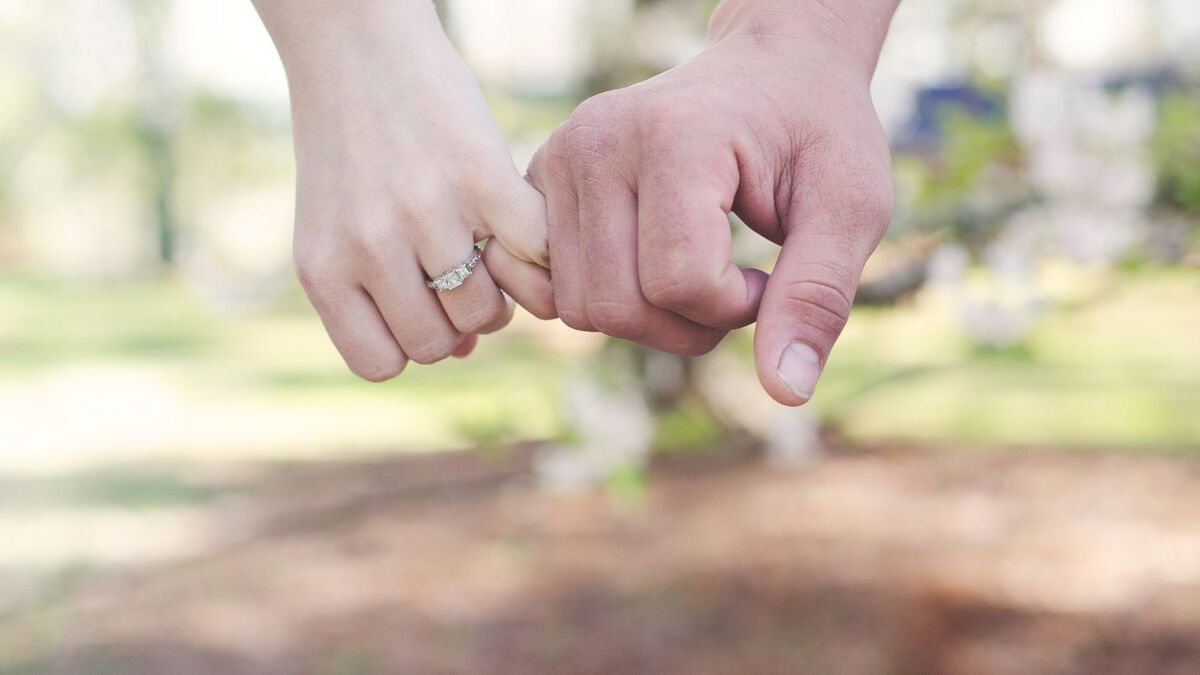 Duas mãos dadas com um anel de noivado.