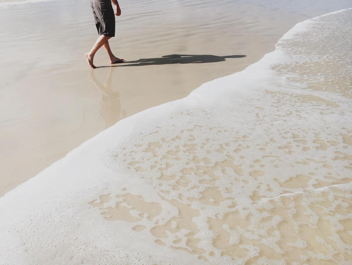 Homem andando na areia da praia.