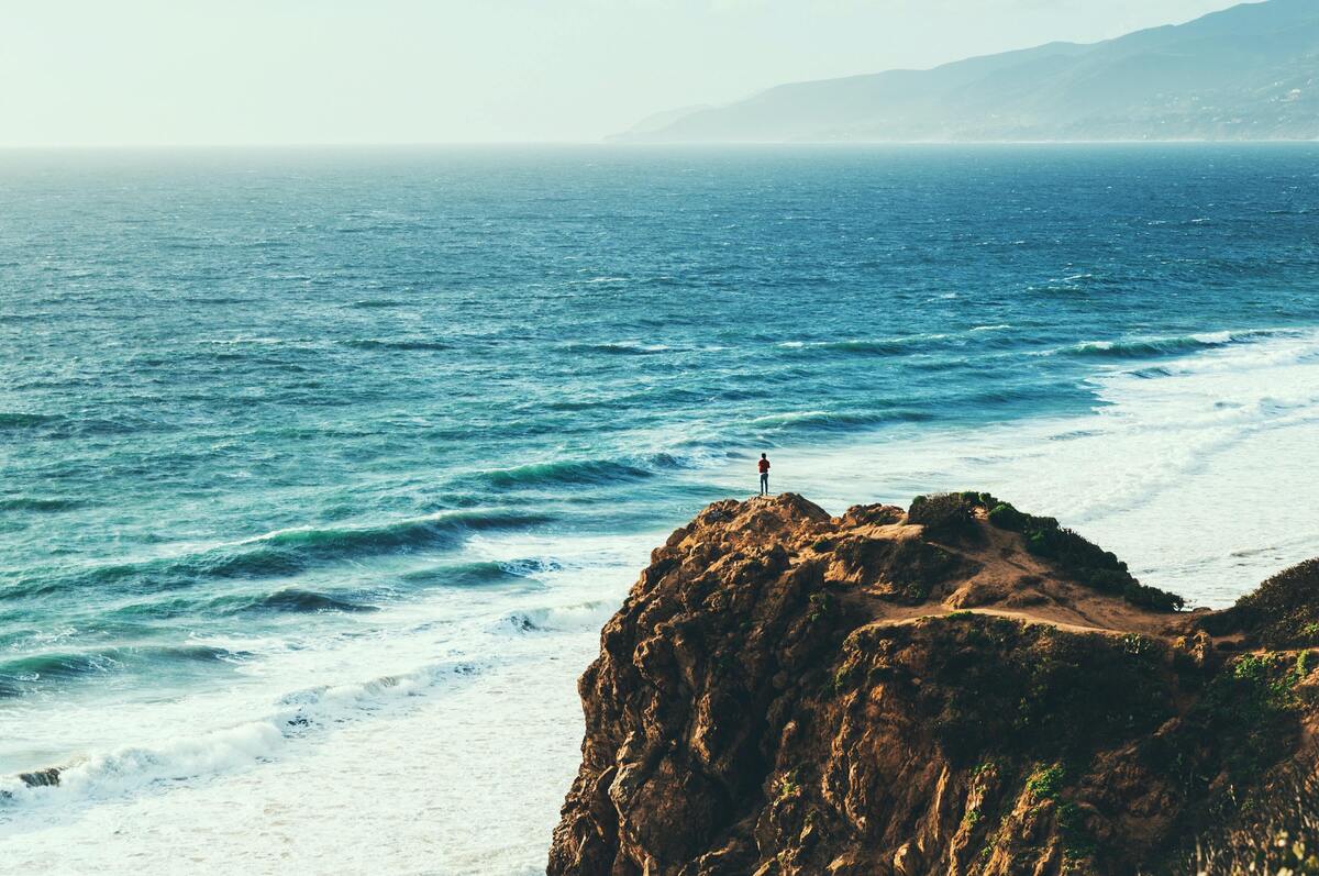 Homem em cima de uma pedra, olhando para o mar.