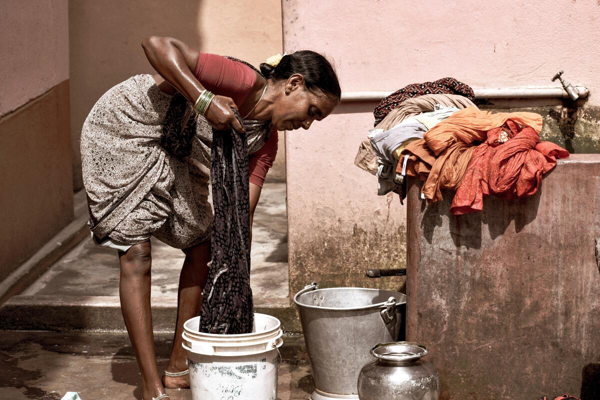 Mulher lavando roupa dentro de baldes.