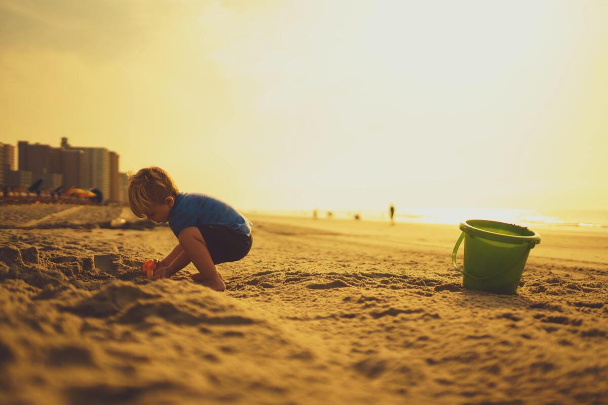 Criança brincando na praia com um balde.