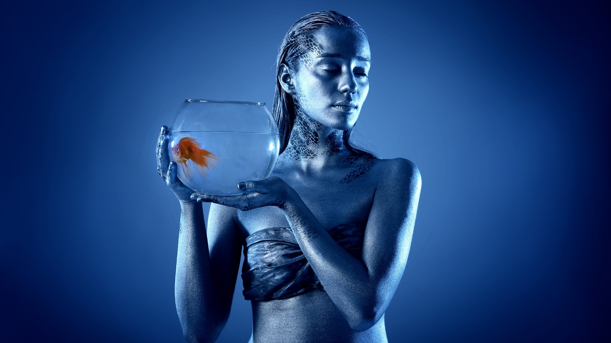Mulher em um fundo azul segurando um aquário.