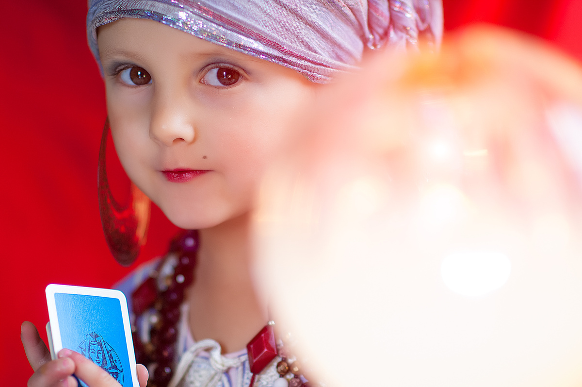 Menina vestida como cigana com carta de Tarot nas mãos e bola de cristal a sua frente