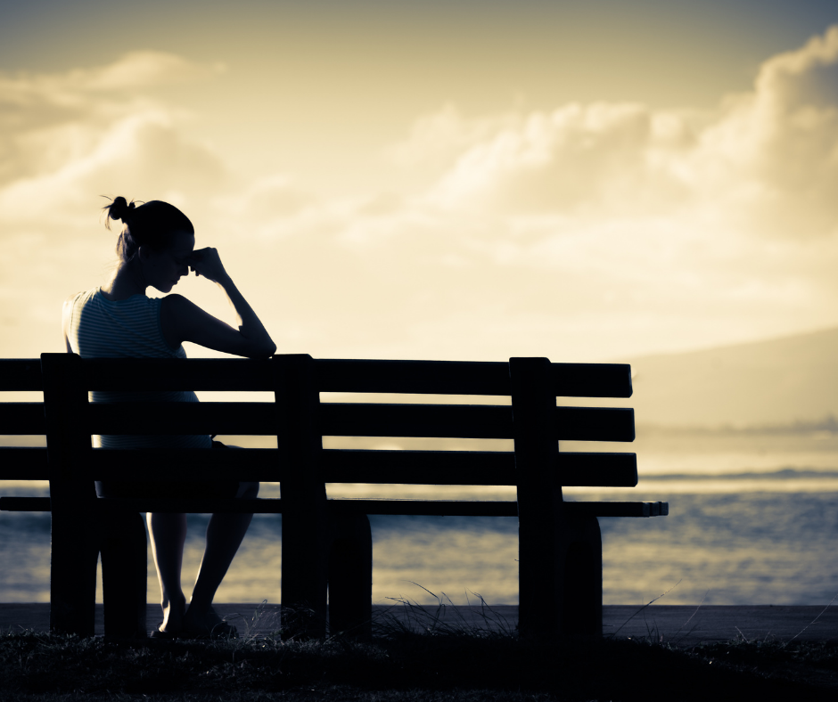 mulher sentada em um banco na frente da praia com uma das mãos na cabeça