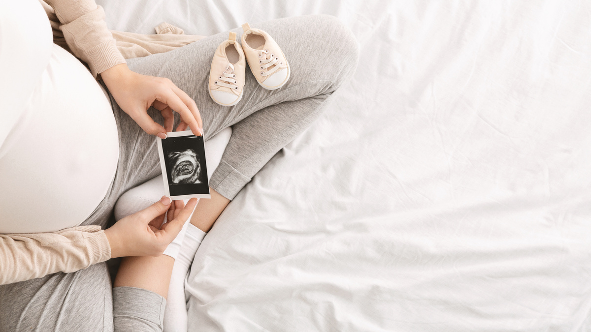 Mulher grávida com celular na mão com ultrassom do bebê e sapatinhos
