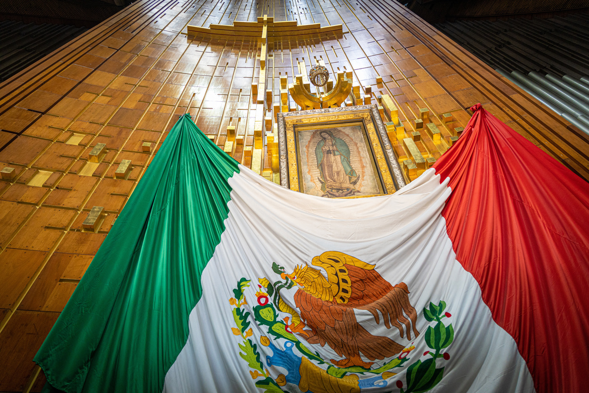 Bandeira do México em frente a pintura de Nossa Senhora de Guadalupe