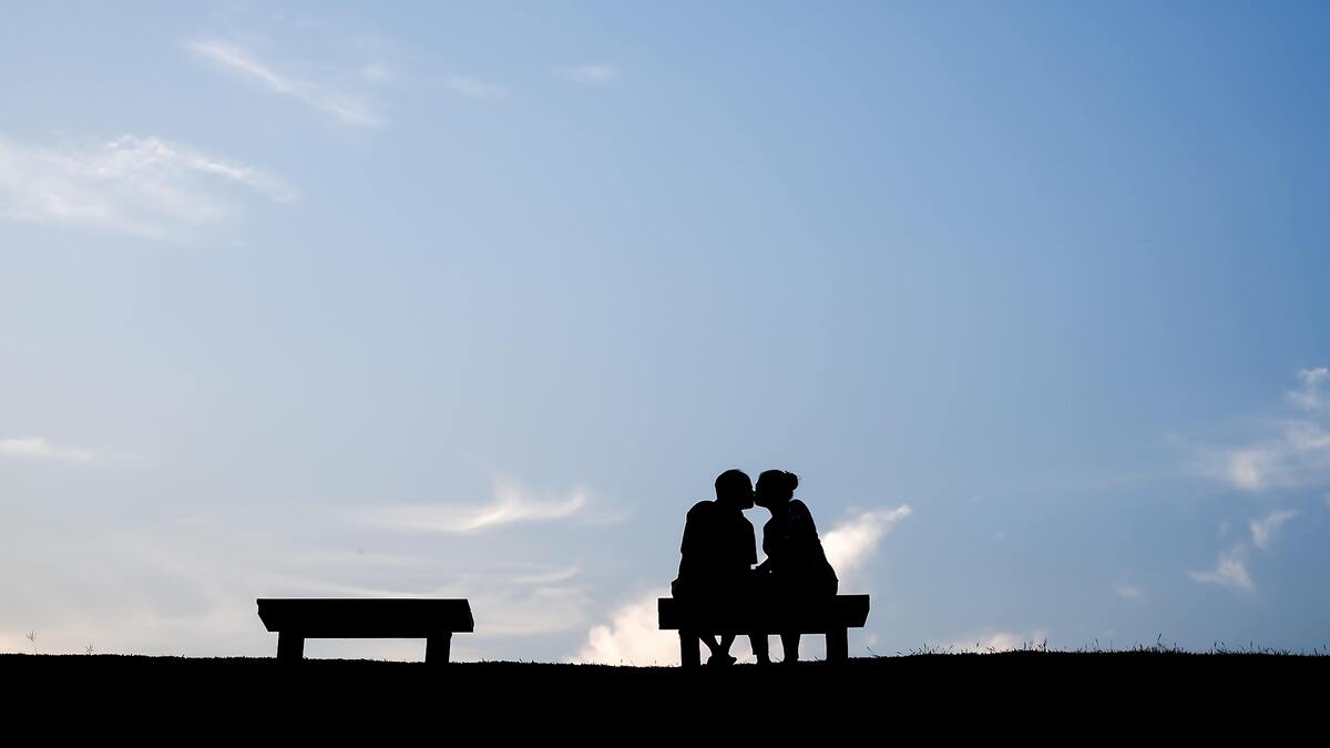 Casal sentado em banco se beijando