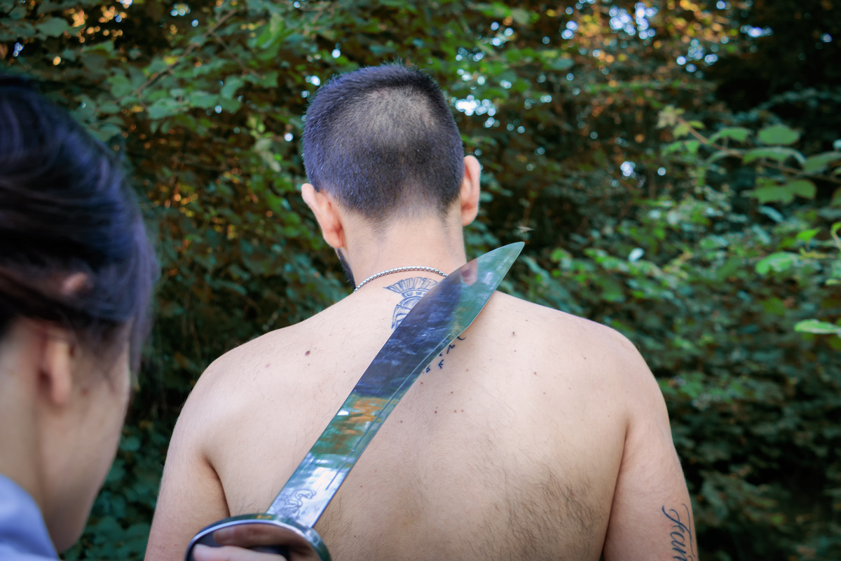 Homem segurando facão na direção do pescoço de outro homem 