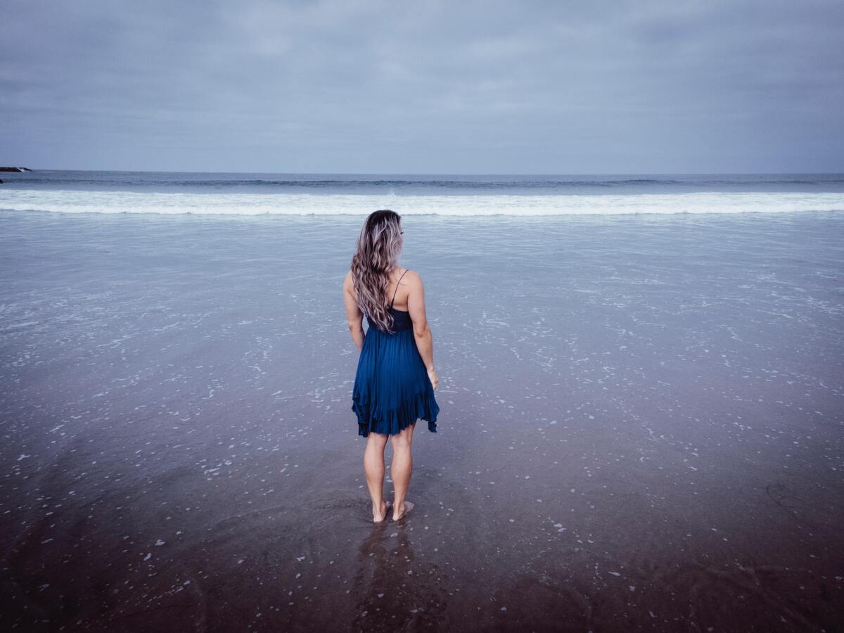 Mulher usando vestido azul na praia.