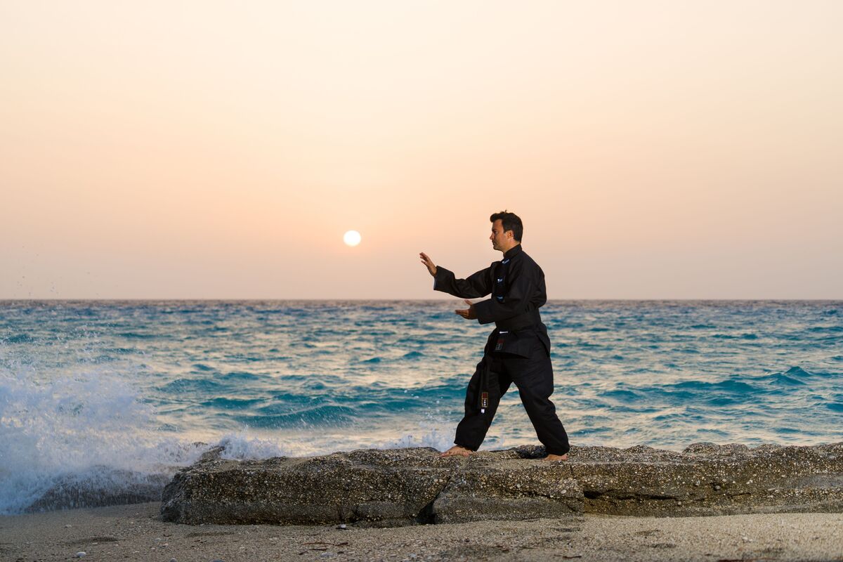 Homem praticando Qigong em praia.