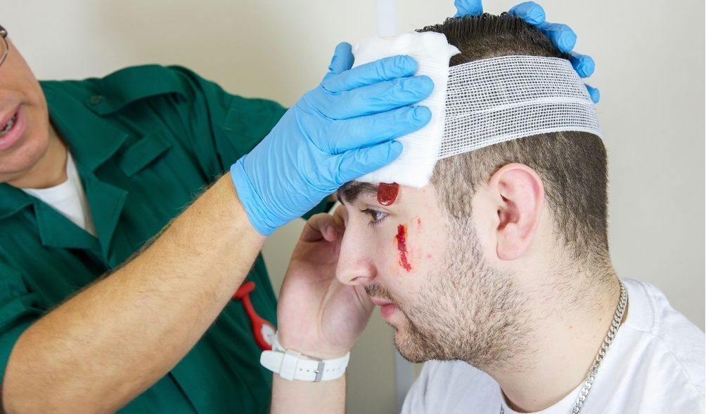 Homem com machucado na cabeça sendo ajudado por paramédico