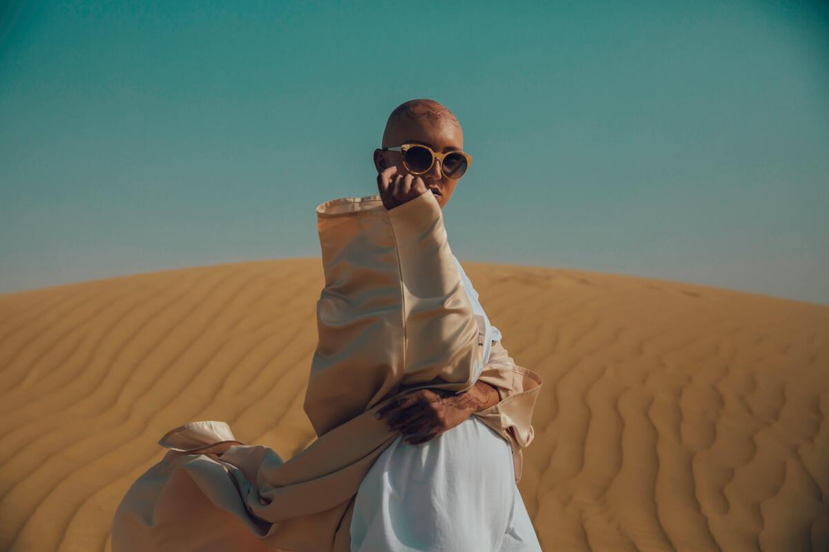 Mulher careca em frente a montanhas de areia.