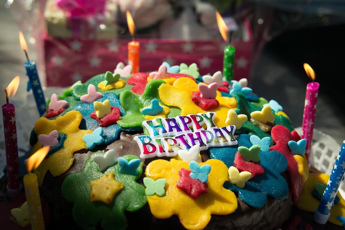 Bolo de aniversário decorado com confeitos coloridos e velas. 