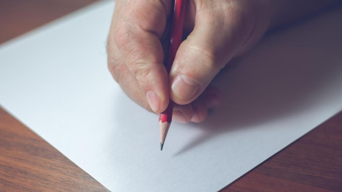 Pessoa escrevendo em um caderno com lápis.