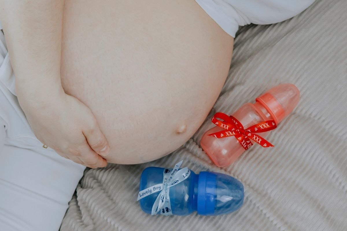 barriga de mulher grávida de gêmeos, com duas mamadeiras ao lado