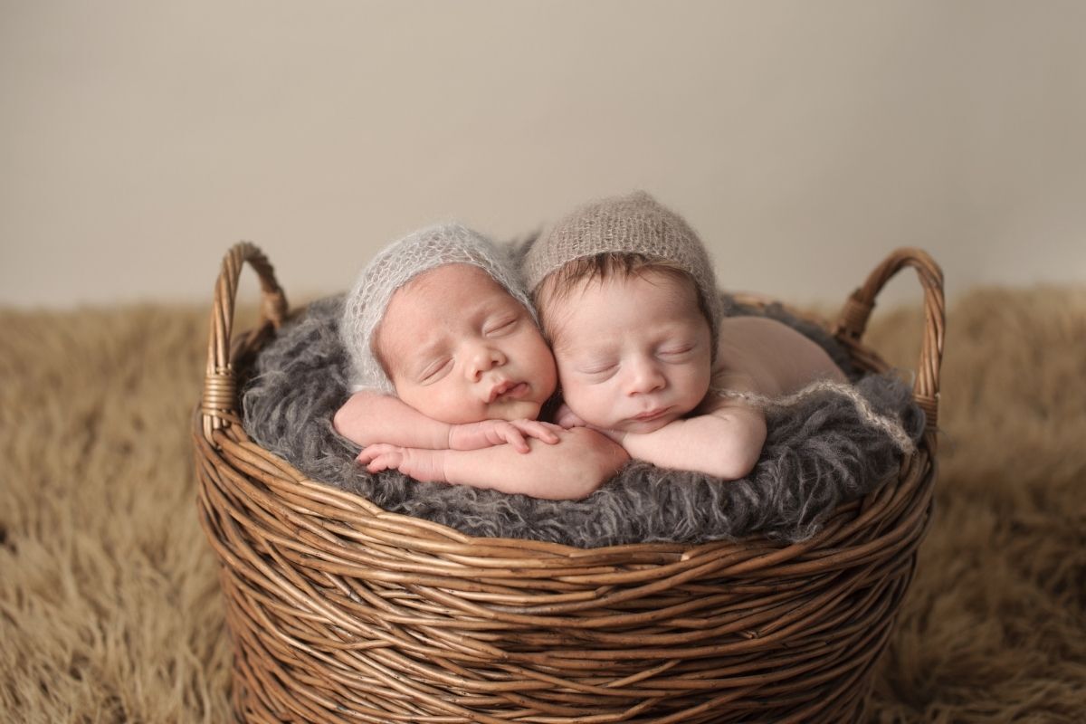 gêmeos recém-nascidos com os olhos fechados e os braços no queixo