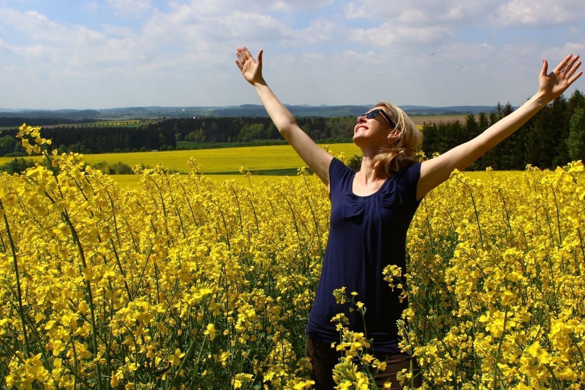 Mulher livre com os braços abertos em um campo de flores amarelas