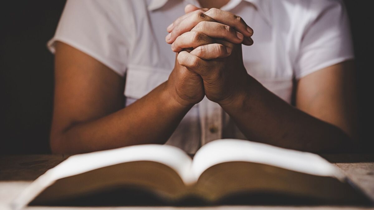 Mãos orando perto de uma bíblia.