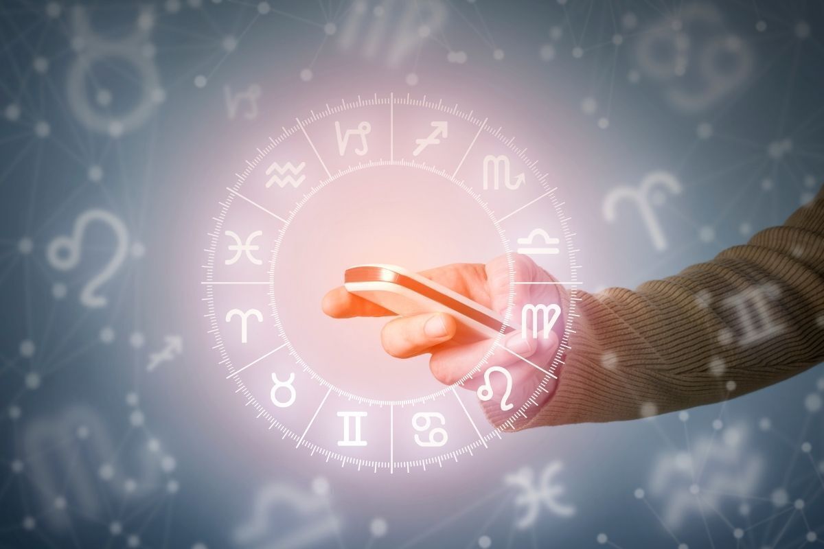 Imagem Ilustrativa - Símbolos dos Signos do zodíaco em círculo neon, pessoa segurando um celular no centro da foto.