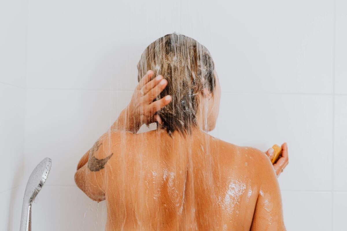Mulher virada de costas, tomando banho de chuveiro.