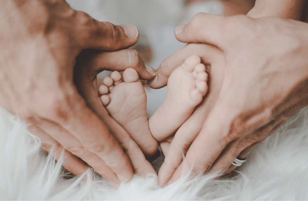 Mãos do pai e da mãe segurando os pés do bebê