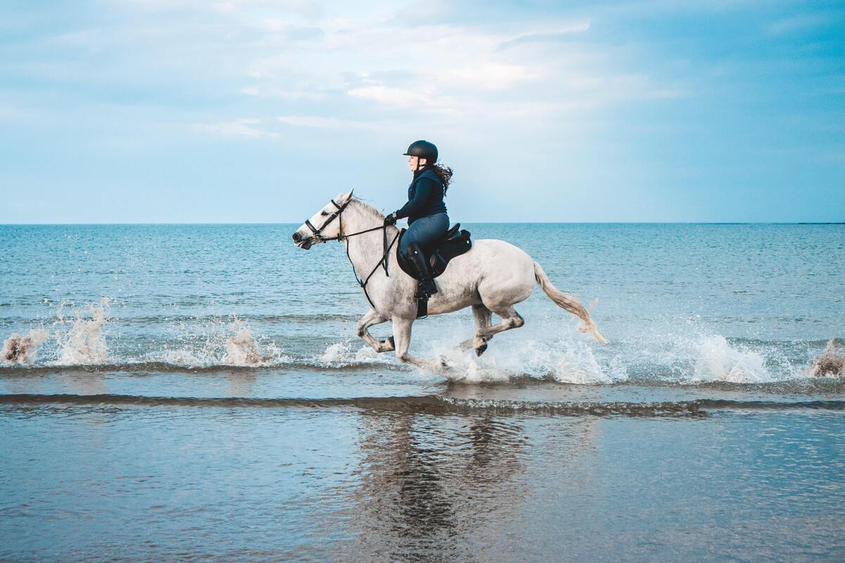 Mulher andando a cavalo na praia.