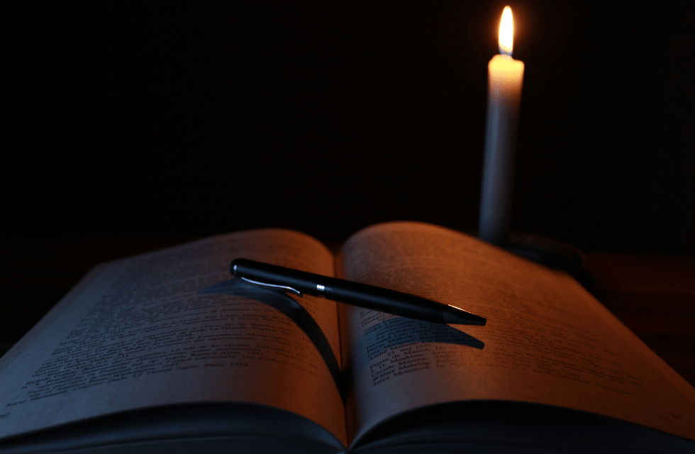 Livro com caneta e uma vela acesa no escuro