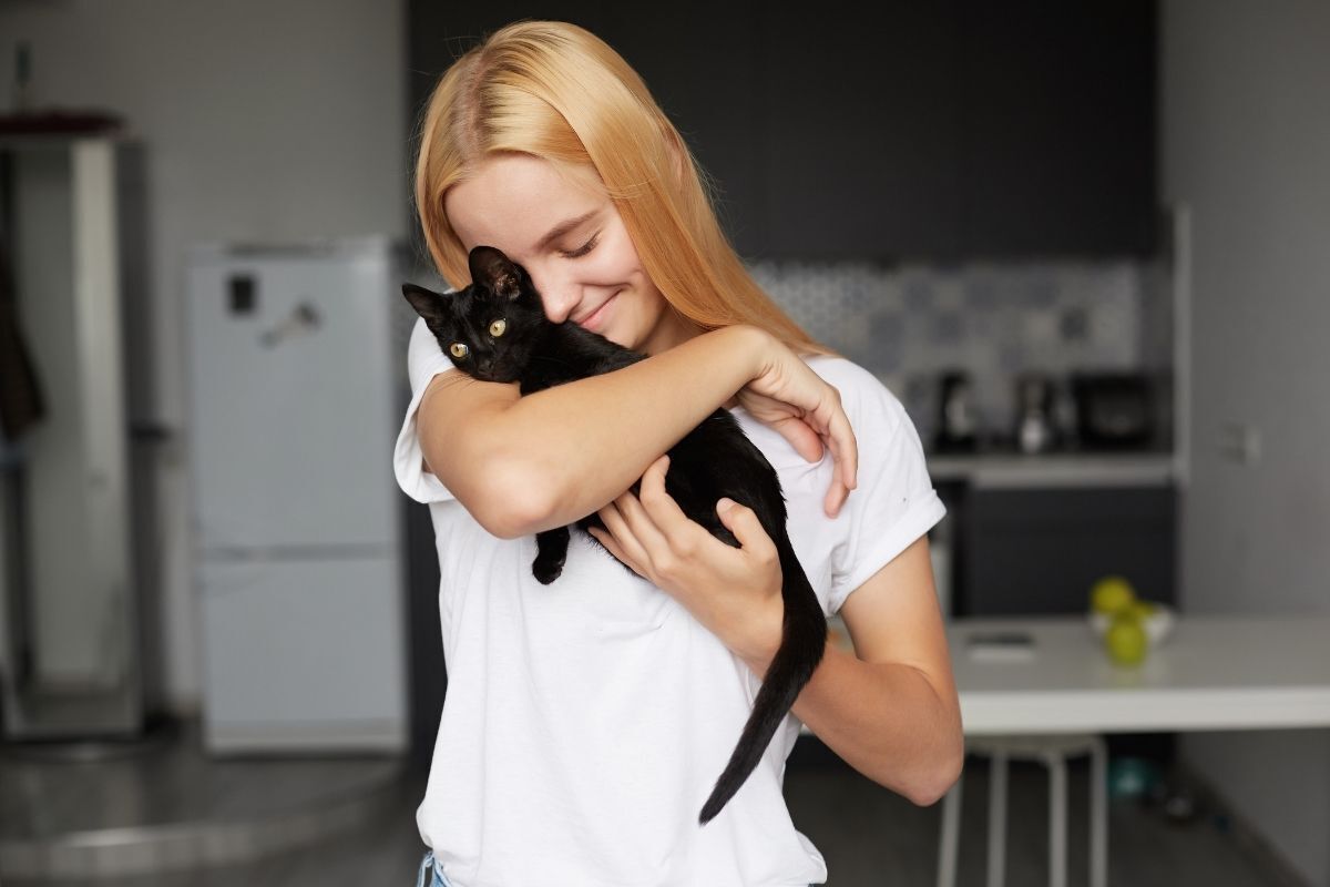 Mulher abraçando gatinho preto e sorrindo