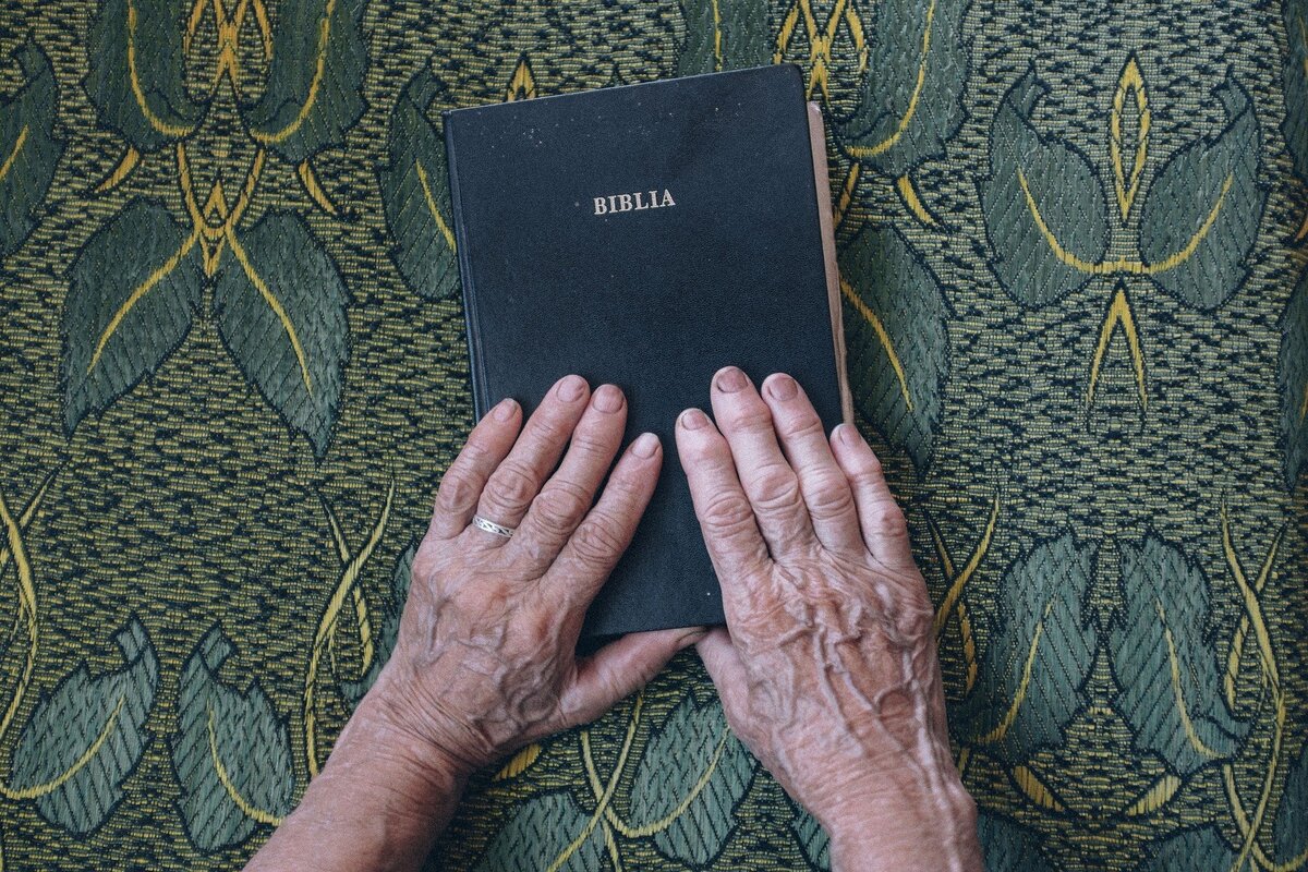 Mãos de pessoa idosa segurando Bíblia, onde o número 12 é encontrado em diversas situações. 