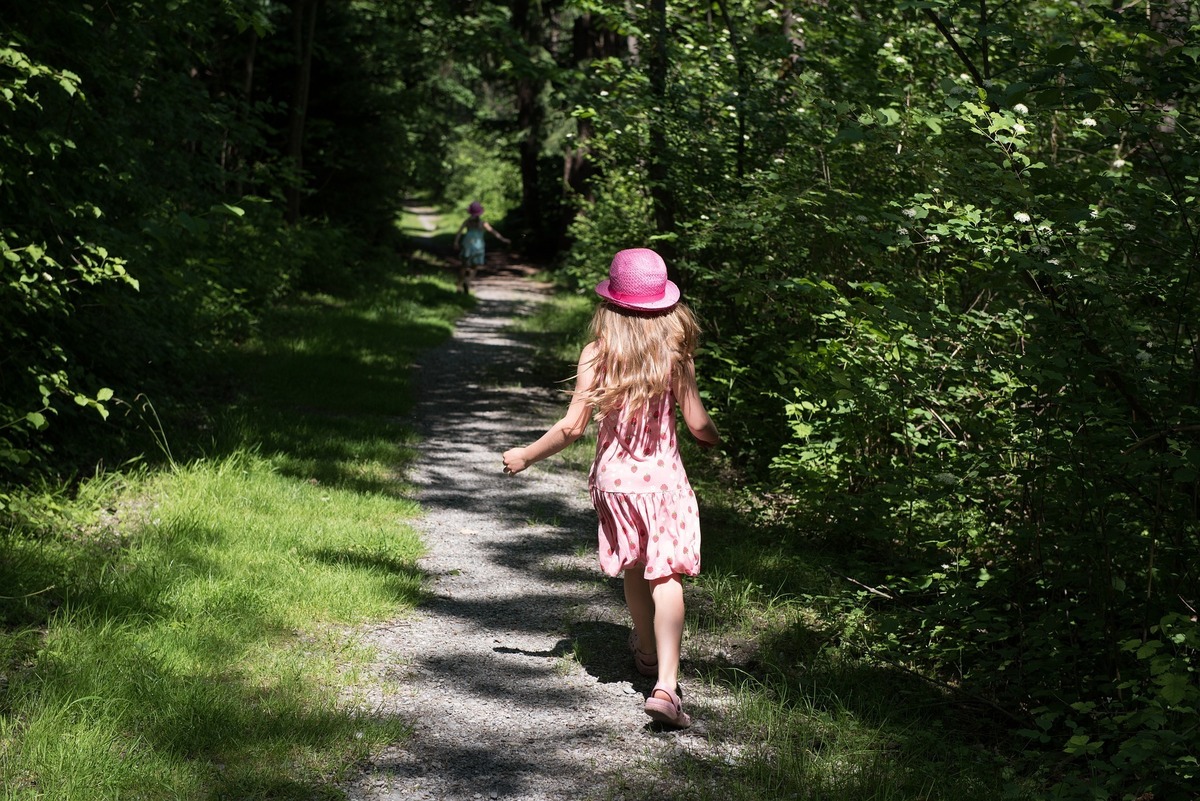 Menina usando chapéu rosa, fugindo para dentro de uma floresta.