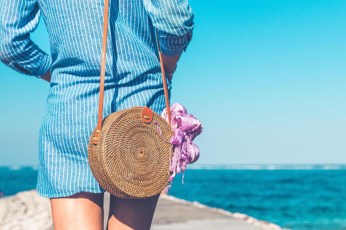 Mulher carregando bolsa pequena com roupa de praia dentro.
