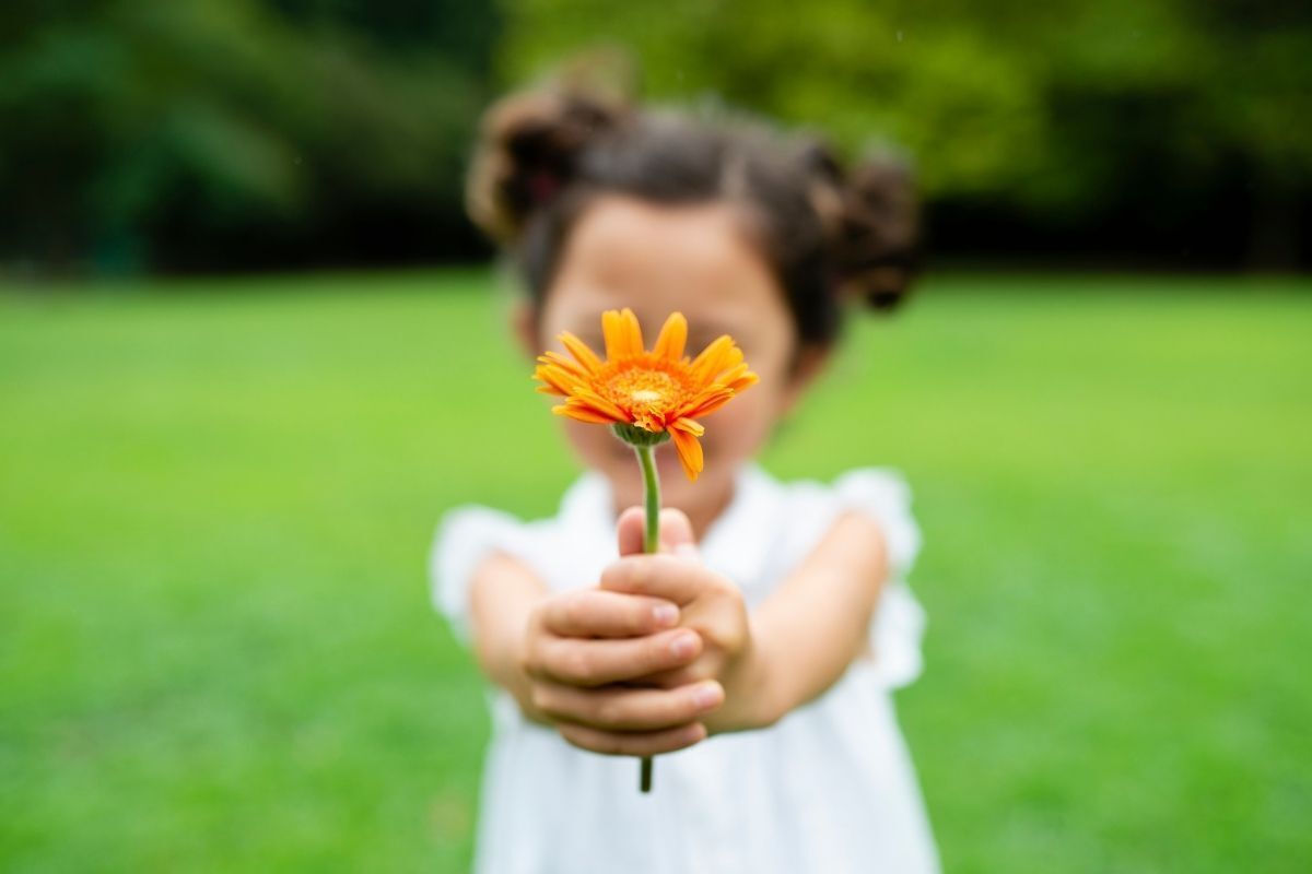 Criança segurando uma flor nas suas mãos, em forma de gratidão.