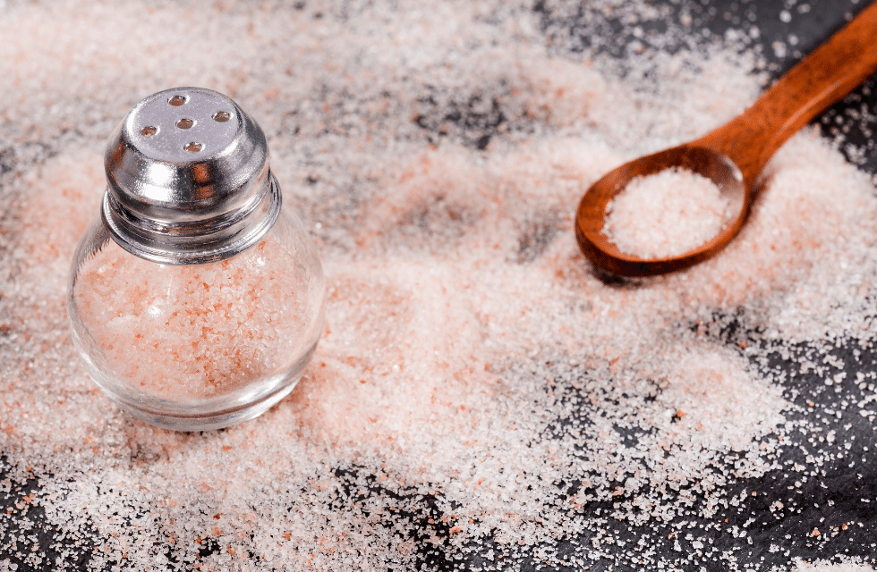 Sal fino derramado sobre a mesa com uma colher e um saleiro