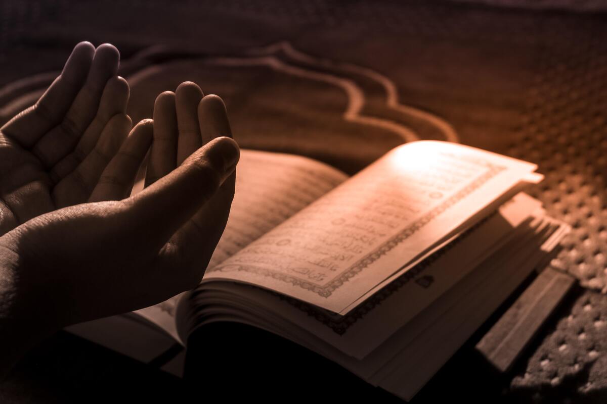 Mãos de uma pessoa rezando e uma bíblia. 