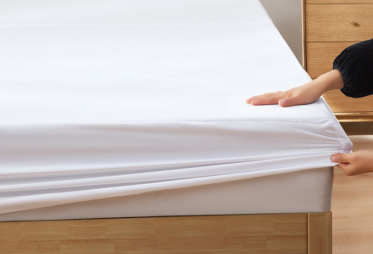 Pessoa terminando de colocar lençol grande em cama de casal. 