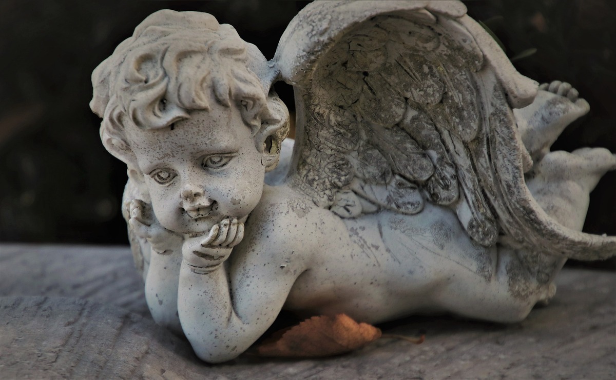 Imagem de anjo querubim com o rosto apoiado nas mãos enquanto se deita. 