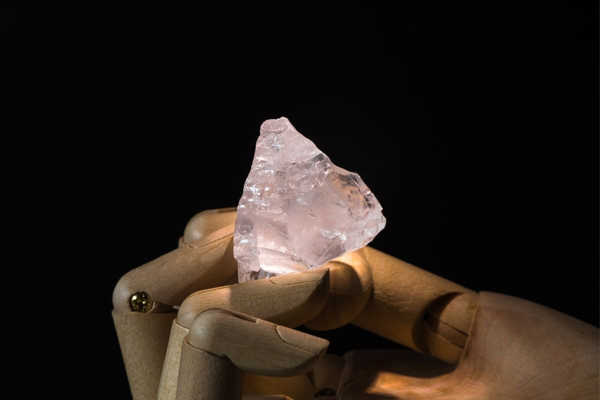 Cristal de Quartzo Rosa com um foco de luz sob ele, situado em uma superfície de madeira, com o fundo escuro.