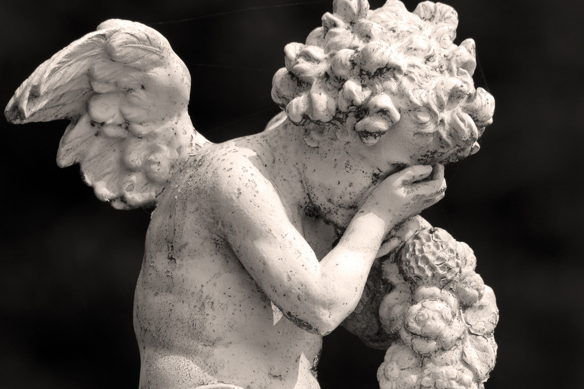 Estátua de anjo querubim cobrindo o rosto enquanto chora. 