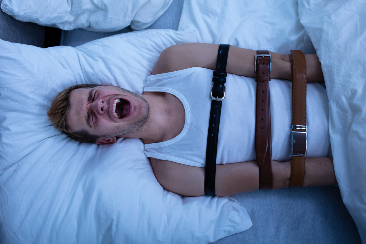Homem acorrentado na cama, sem poder se mexer, simbolizando a paralisia do sono. 
