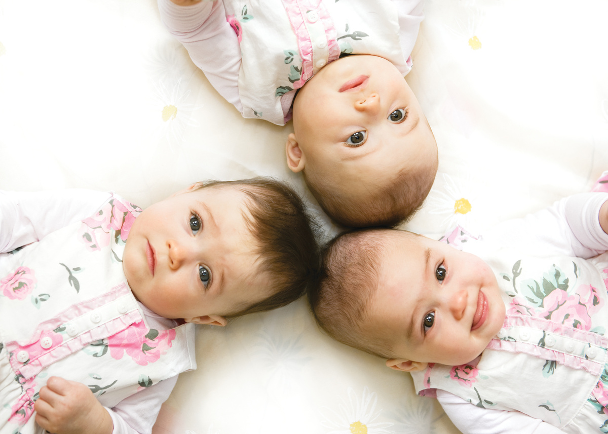 Bebês trigêmeos deitados de costas um para o outro, em fundo branco.