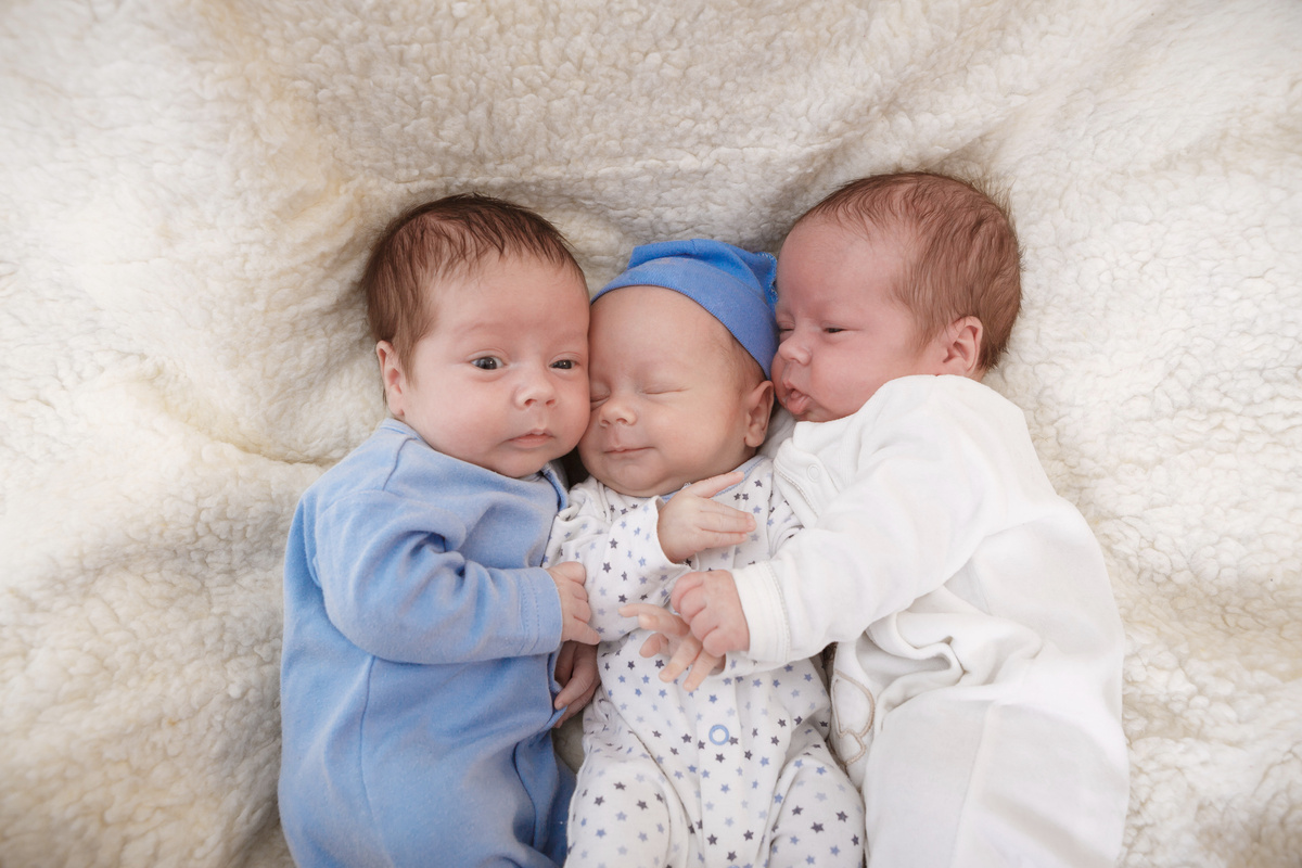 Trigêmeos recém-nascidos se abraçando enquanto deitam. 